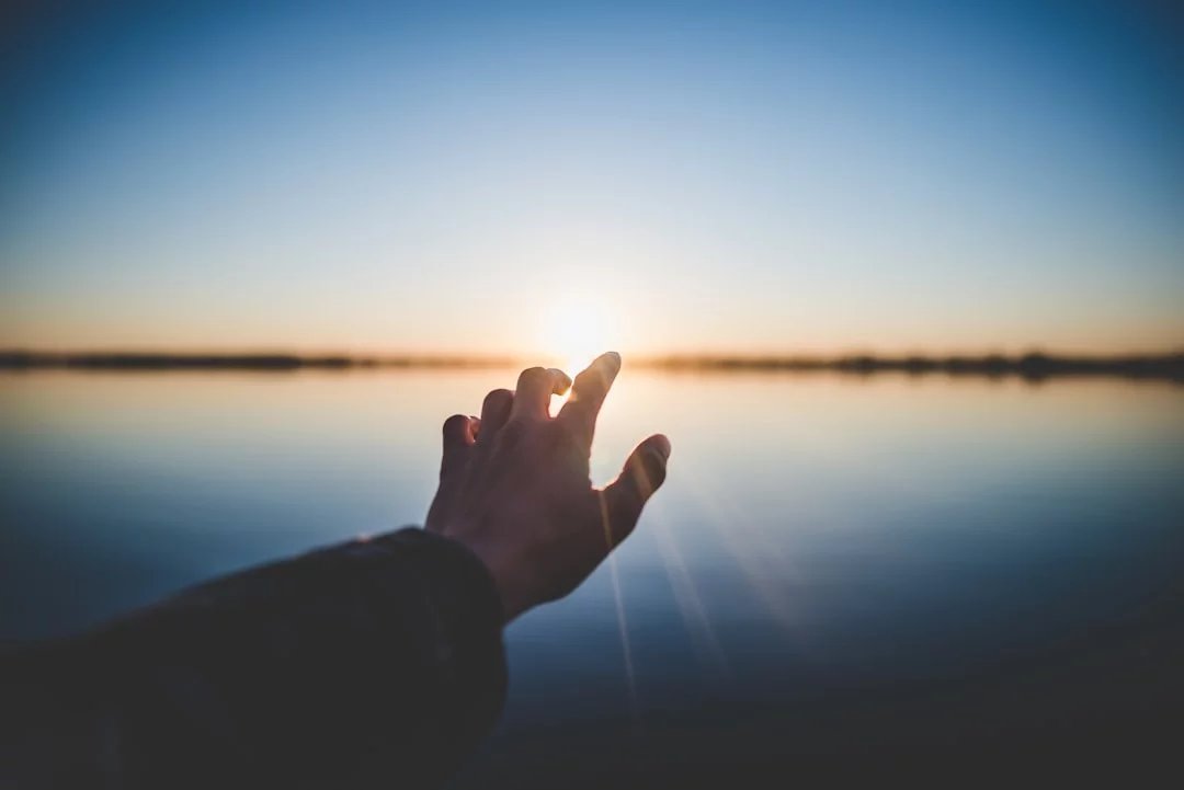 mão_e_antebraco_a_apontar_para_o_sol_num_final_de_tarde_num_lago